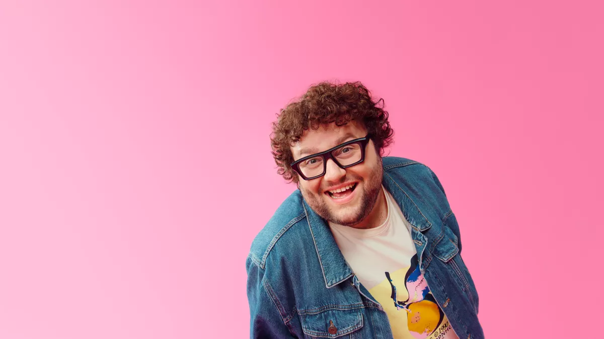 Manu Van Acker sonriendo frente a un micrófono con el logo de MNM Radio en el fondo